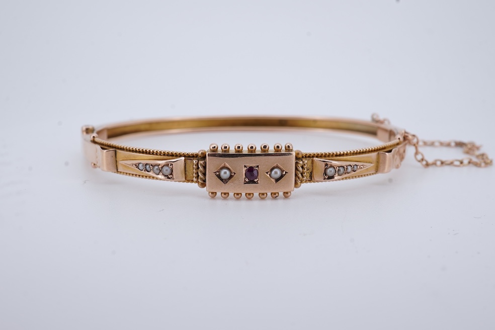 An Edwardian 9ct, seed pearl and ruby set hinged bangle, interior diameter 57mm, gross weight 8.3 grams. Condition - poor to fair